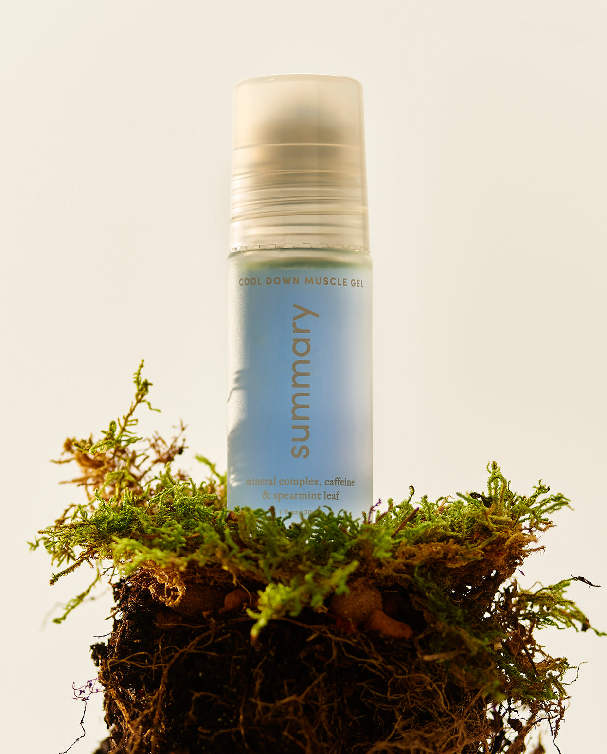 A roll-on bottle of COOL DOWN MUSCLE GEL with a stainless-steel roller-ball applicator, placed on a bed of moss.