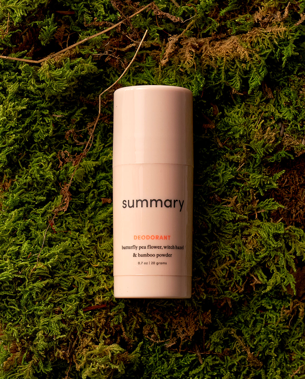 A travel-friendly mini size deodorant stick placed on a green mossy surface.