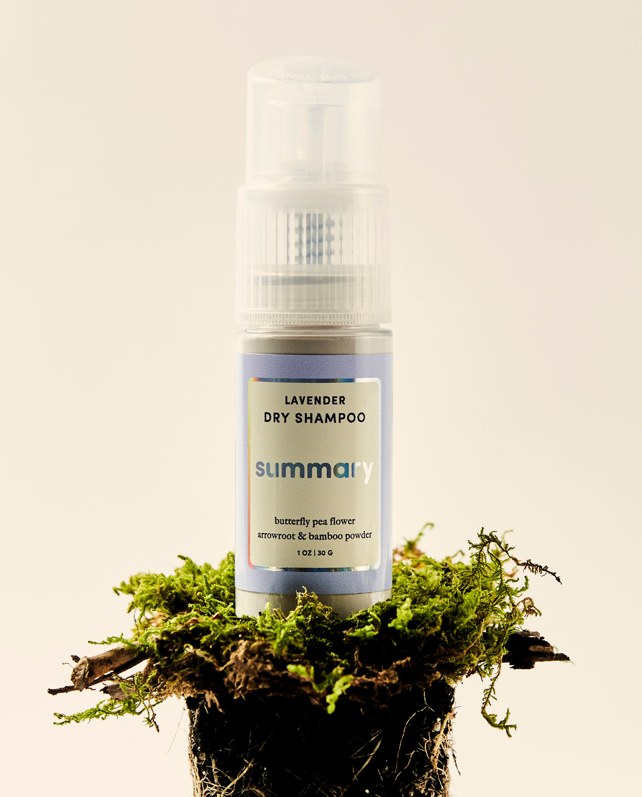 A bottle of dry shampoo powder with a lavender label, placed on a bed of moss.