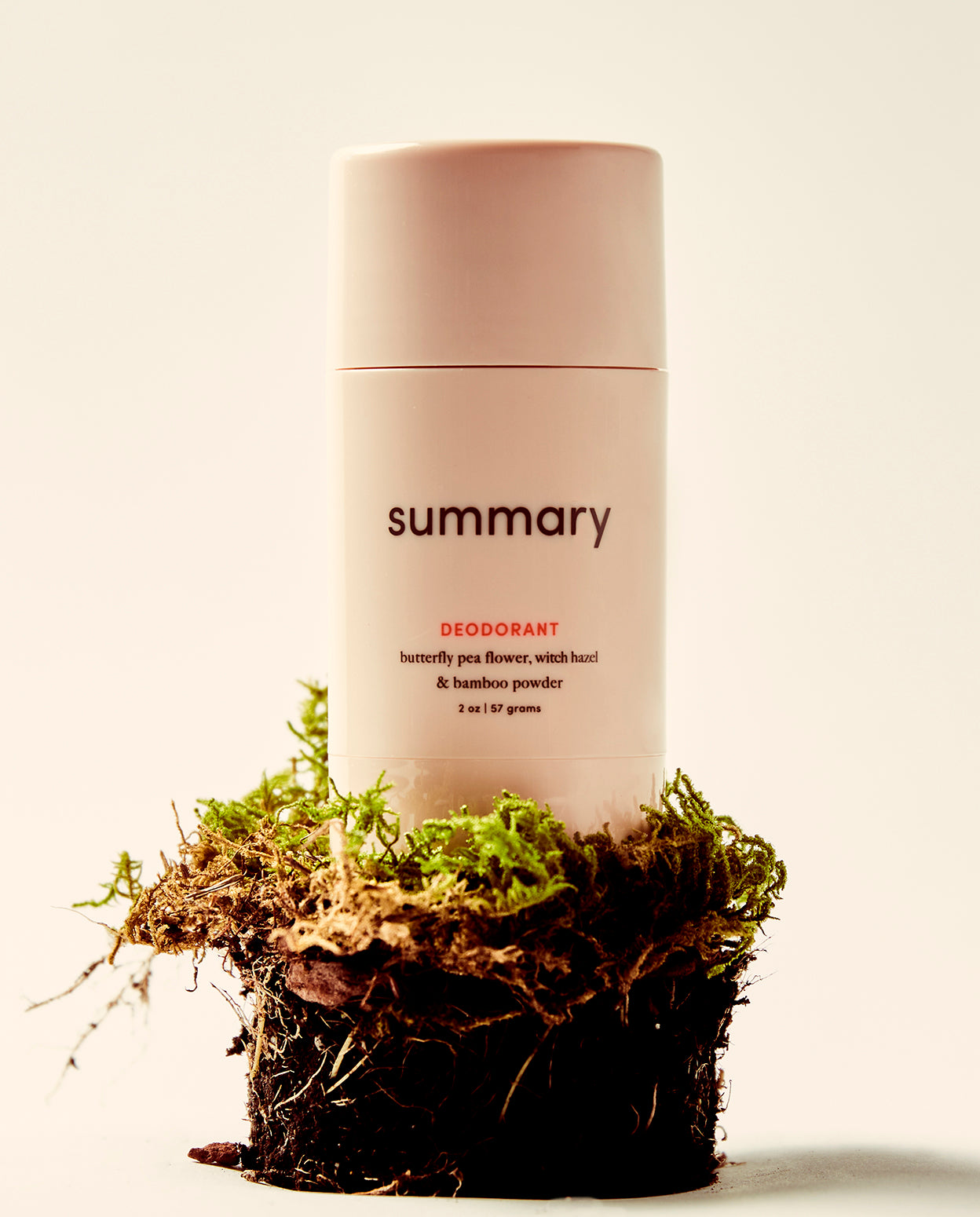 A stick deodorant with 'summary' branding placed on a bed of moss. The deodorant stick is pink in color and the product is identified as 'DEODORANT' in the image description.