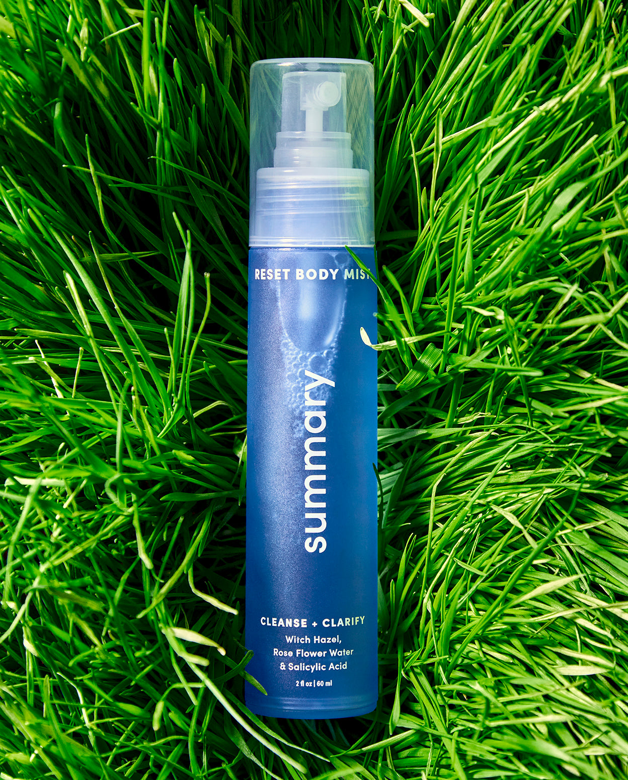 A bottle of 'RESET BODY MIST' by SUMMARY placed on a grassy surface.